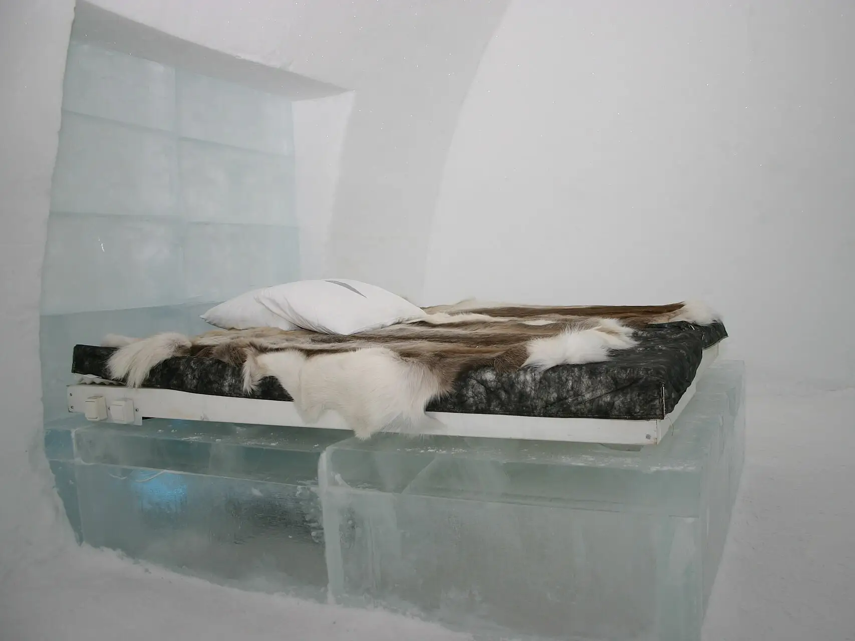Een bed van ijsblokken met rendiervellen in een kamer van het Icehotel
